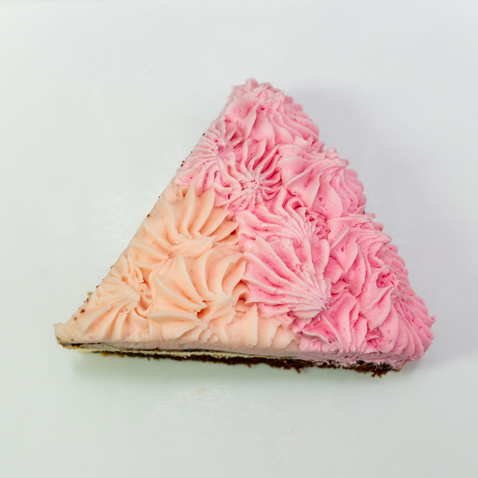 Slice of cheesecake topped with piped pink and peach frosting, displayed against a plain white background.