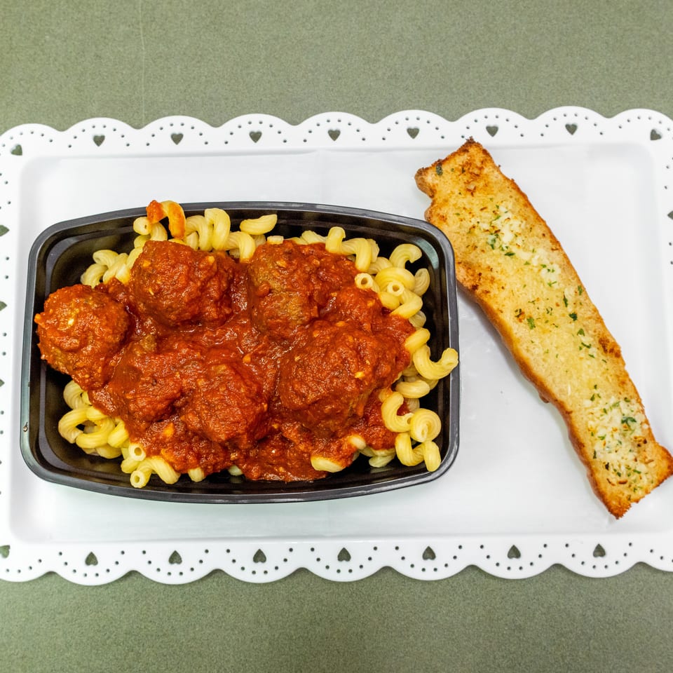 Tray of curly pasta topped with meatballs and tomato sauce, served with garlic bread on a decorative white platter.