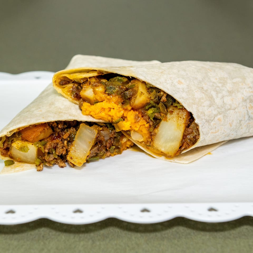 Two flour tortillas filled with seasoned meat, potatoes, vegetables, and orange rice, served on a white tray.